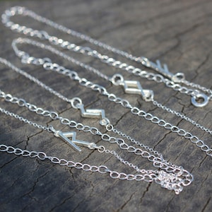 May include: Five silver chain necklaces with lightning bolt pendants. The chains are delicate and the pendants are simple and modern.