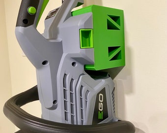May include: A gray and green electric hedge trimmer with a black handle and a green wall mount. The trimmer has the word "EGO" printed on the side.