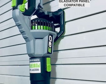 May include: An EGO Power+ 765 CFM blower mount, compatible with Gladiator panels. The handheld blower is primarily gray and black, with green accents. The text "EGO POWER+ 765 CFM BLOWER MOUNT GLADIATOR PANEL COMPATIBLE" is visible.