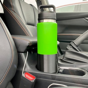 May include: A green and black insulated water bottle with a carrying handle sits in the cup holder of a car.