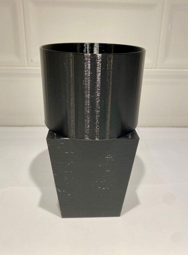 Peut inclure: Un pot de fleurs noir imprim&eacute; en 3D avec un dessus cylindrique et une base carr&eacute;e.