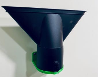 May include: A black and green plastic object, possibly a tool attachment, mounted on a wall. The object has a wide, angled top, a cylindrical midsection, and a green base. The design suggests it may be for directing airflow or similar function.