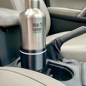 May include: A silver stainless steel water bottle with a black lid and a green logo that says "klean kanteen insulated" in a car cup holder.