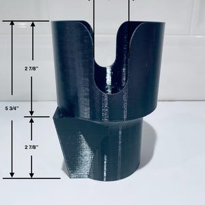 May include: Black, 3D-printed cup holder with a unique design. The holder is 5 3/4 inches tall, with a top opening of 1 inch. The upper cup section is 2 7/8 inches tall, and the base is also 2 7/8 inches tall. The holder has a distinctive angled base.