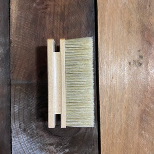 May include: A wooden brush with a natural bristle brush head. The brush is in a wooden holder.