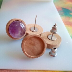 Peut inclure: Une paire de supports d'oreille en bois avec un cabochon d'améthyste violet dans l'un des supports. Les supports sont ronds et ont une finition en bois naturel lisse. Les tiges de boucles d'oreilles sont en métal argenté.