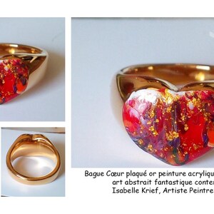May include: Gold-plated ring with a heart-shaped centerpiece. The heart features a vibrant abstract design in red, gold, and purple hues. The ring's band is a polished gold color. The image includes the text: Bague C&oelig;ur plaqu&eacute; or peinture acrylique et poudre d'or, art abstrait fantastique contemporain, Isabelle Krief, Artiste Peintre auteure.