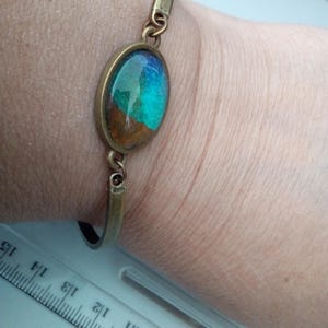 May include: A bronze bangle bracelet with a blue, green and brown oval resin cabochon.