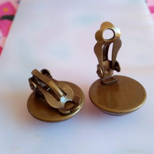 Pu&ograve; includere: Un paio di orecchini a clip color bronzo con un design rotondo e piatto. Gli orecchini hanno uno stile semplice ed elegante.