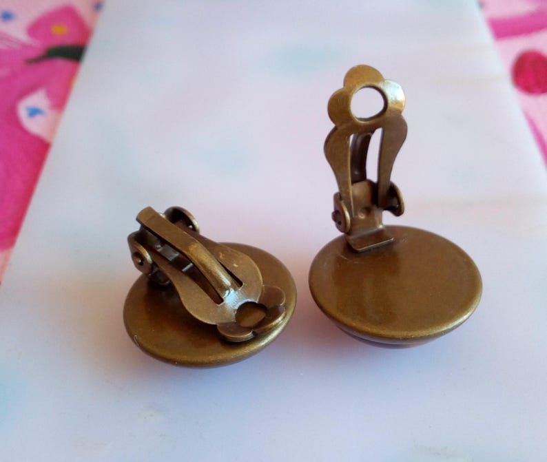 Pu&ograve; includere: Un paio di orecchini a clip color bronzo con un design rotondo e piatto. Gli orecchini hanno uno stile semplice ed elegante.