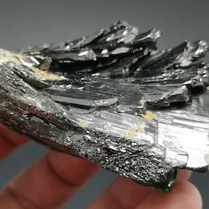 May include: A black, metallic, rough-textured mineral specimen with a layered, striated appearance. The mineral has a dark, almost silver-like sheen.