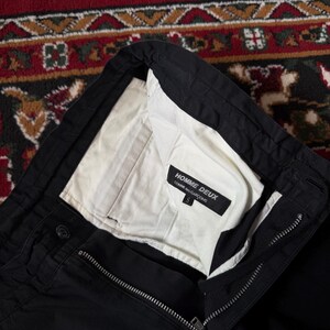 May include: Black trousers with a white lining visible at the waist. The trousers feature a zip and button fastening. The label inside reads "HOMME DEUX COMME des GAR&Ccedil;ONS". Size S.