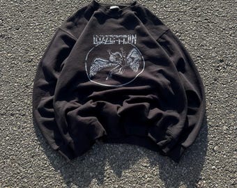 Może przedstawiać: Czarny, dług rękawowy sweter z białym nadrukiem graficznym przedstawiającym skrzydlatą istotę i tekstem "Led Zeppelin" w kółku.