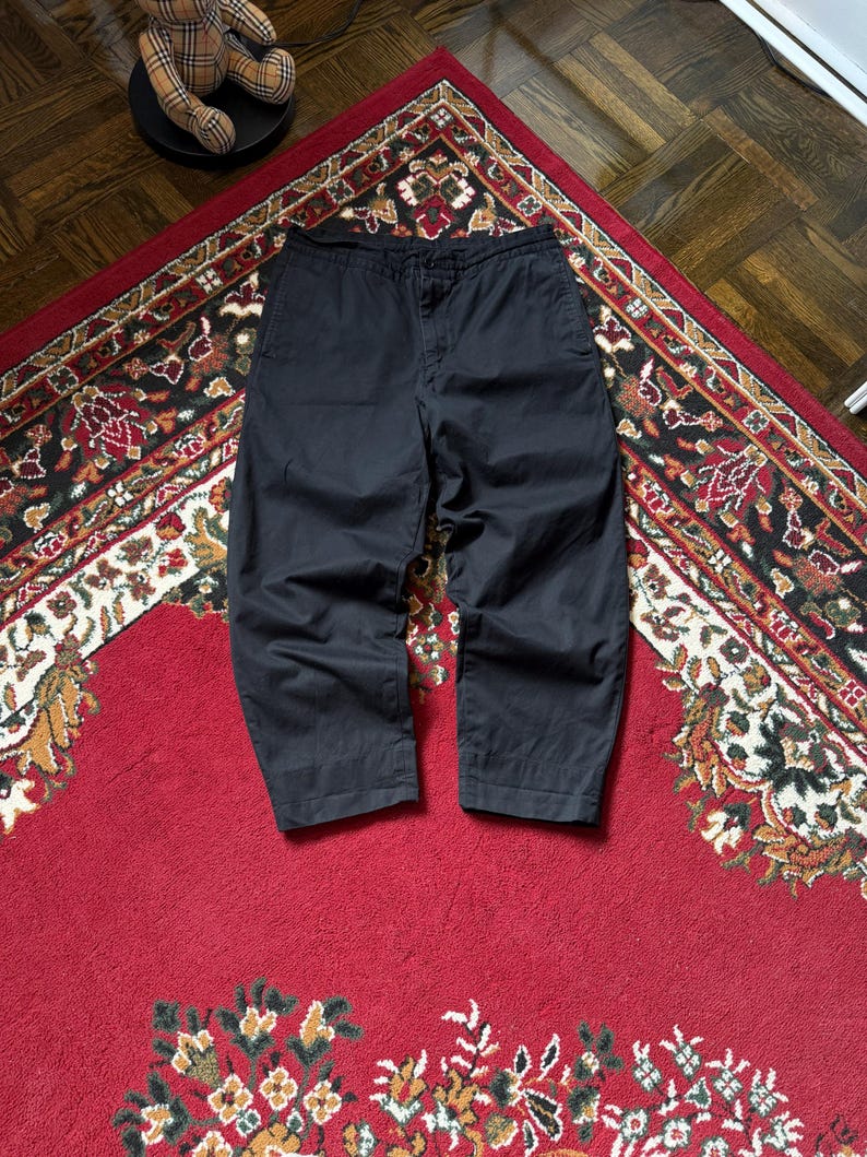 May include: A white ceramic mug with a black handle and the text "But First, Coffee" in a handwritten style. The mug is on a white surface. The mug is approximately 10 cm tall.