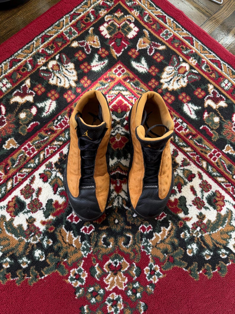 Op de afbeelding: Een paar bruin en zwarte Jordan 13 sneakers. De schoenen hebben een bruin su&egrave;de bovenwerk met zwarte accenten op de neus en veters. De zolen zijn zwart en het Jumpman-logo is zichtbaar op de tong.