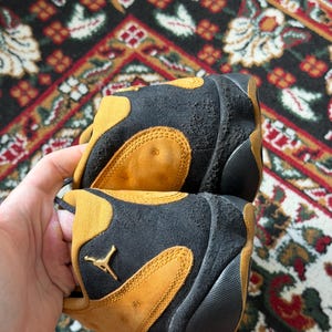 Op de afbeelding: Een witte keramische mok met een zwarte handgreep en de tekst "But First, Coffee" in een vetgedrukte, zwarte letter. De mok staat tegen een vage achtergrond. De mok is ongeveer 10 cm hoog.