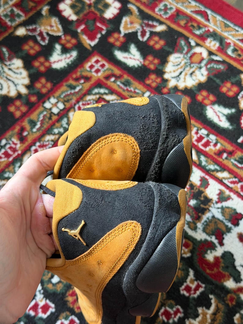 Op de afbeelding: Een witte keramische mok met een zwarte handgreep en de tekst "But First, Coffee" in een vetgedrukte, zwarte letter. De mok staat tegen een vage achtergrond. De mok is ongeveer 10 cm hoog.