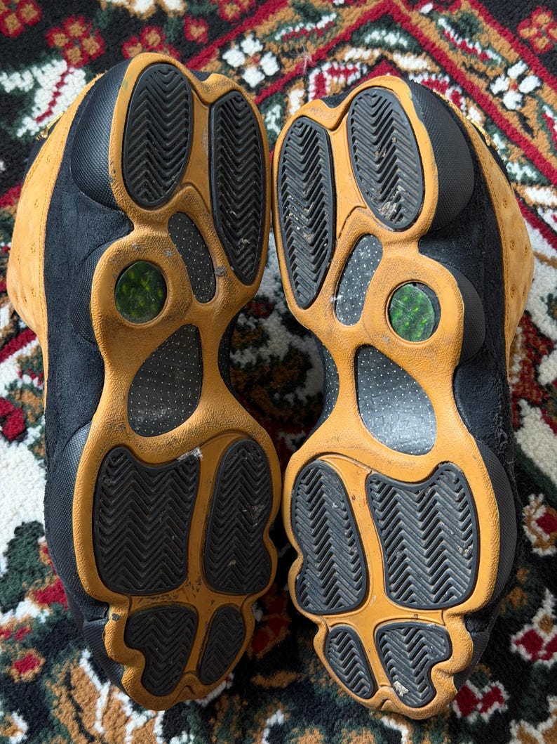 Op de afbeelding: Paar zwarte en bruine sneakers met een textuurzool. De zolen zijn bruin met zwarte rubberen profielen. De schoenen zijn versleten.