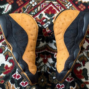 Op de afbeelding: Paar zwarte en bruin-gele sneakers. De schoenen hebben een bruin-geel bovenwerk met een geperforeerd patroon en zwarte details. De zolen zijn zwart en de sneakers zijn geregen.