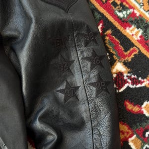 Może przedstawiać: Biały ceramiczny kubek z czarnym uchwytem i napisem "But First, Coffee" w stylu odręcznym. Kubek stoi na białej powierzchni. Kubek ma około 10 cm wysokości.