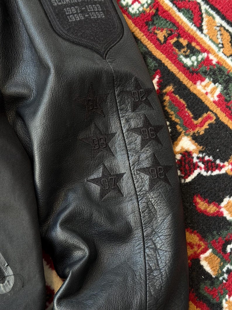 Może przedstawiać: Biały ceramiczny kubek z czarnym uchwytem i napisem "But First, Coffee" w stylu odręcznym. Kubek stoi na białej powierzchni. Kubek ma około 10 cm wysokości.