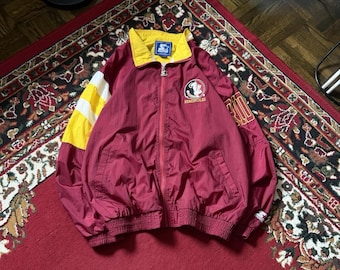 May include: A maroon Starter jacket with a yellow collar and accents. The jacket features a full zip, the Florida State Seminoles logo, and a yellow and white sleeve. The jacket is laid out on a red rug.