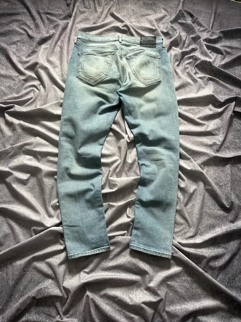 May include: Light blue denim jeans with a faded wash. The jeans have a classic five-pocket design, a leather patch on the back, and a straight leg fit. The back pockets feature a distinctive stitched design.