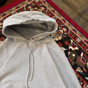 Pu&ograve; includere: Una felpa con cappuccio grigio chiaro con coulisse e cappuccio. La felpa con cappuccio &egrave; realizzata in un materiale morbido e si trova su un tappeto fantasia. La felpa con cappuccio ha una vestibilit&agrave; ampia e maniche lunghe.