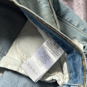 May include: Close-up of light blue denim jeans with a white tag. The tag reads "MADE IN MEXICO" and lists the fabric composition as 99% cotton and 1% elastane. The jeans have visible stitching and a worn appearance.