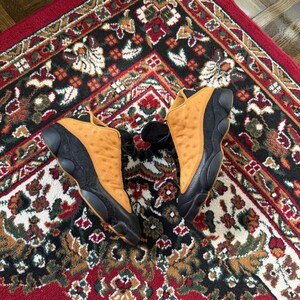 Op de afbeelding: Witte keramische mok met een zwart oor en de tekst "But First, Coffee" in een vetgedrukte, zwarte letter. De mok staat tegen een vage achtergrond, wat een gezellige omgeving suggereert.