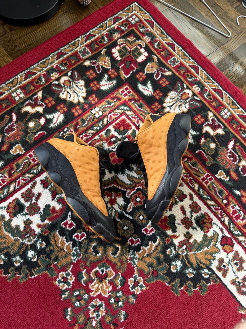 Op de afbeelding: Witte keramische mok met een zwart oor en de tekst "But First, Coffee" in een vetgedrukte, zwarte letter. De mok staat tegen een vage achtergrond, wat een gezellige omgeving suggereert.