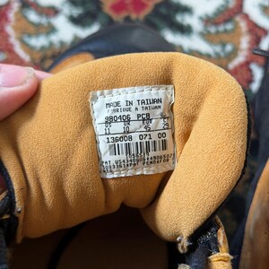 Op de afbeelding: Close-up van de binnenkant van een bruine en zwarte sneaker. De binnenkant heeft een bruine voering en een wit label met zwarte tekst. Het label bevat de tekst "MADE IN TAIWAN" en maat informatie.