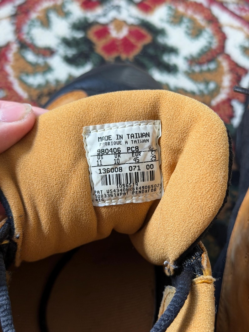Op de afbeelding: Close-up van de binnenkant van een bruine en zwarte sneaker. De binnenkant heeft een bruine voering en een wit label met zwarte tekst. Het label bevat de tekst "MADE IN TAIWAN" en maat informatie.