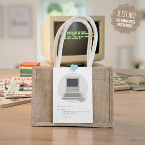 Könnte beinhalten: Eine Geschenk-Tasche aus Jute mit weißen Seilgriffen und einem Anhänger mit einer Vintage-Computer-Illustration und Code. Der Anhänger wird von einer herzförmigen blauen Klammer gehalten. Ein Vintage-Computermonitor ist im Hintergrund zu sehen.