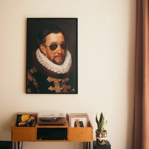 May include: A vintage-style portrait of a man wearing sunglasses and a large white collar, framed in black, hangs on a white wall above a wooden record player stand with a turntable and vinyl records. A potted snake plant sits on a black stand to the right of the record player.