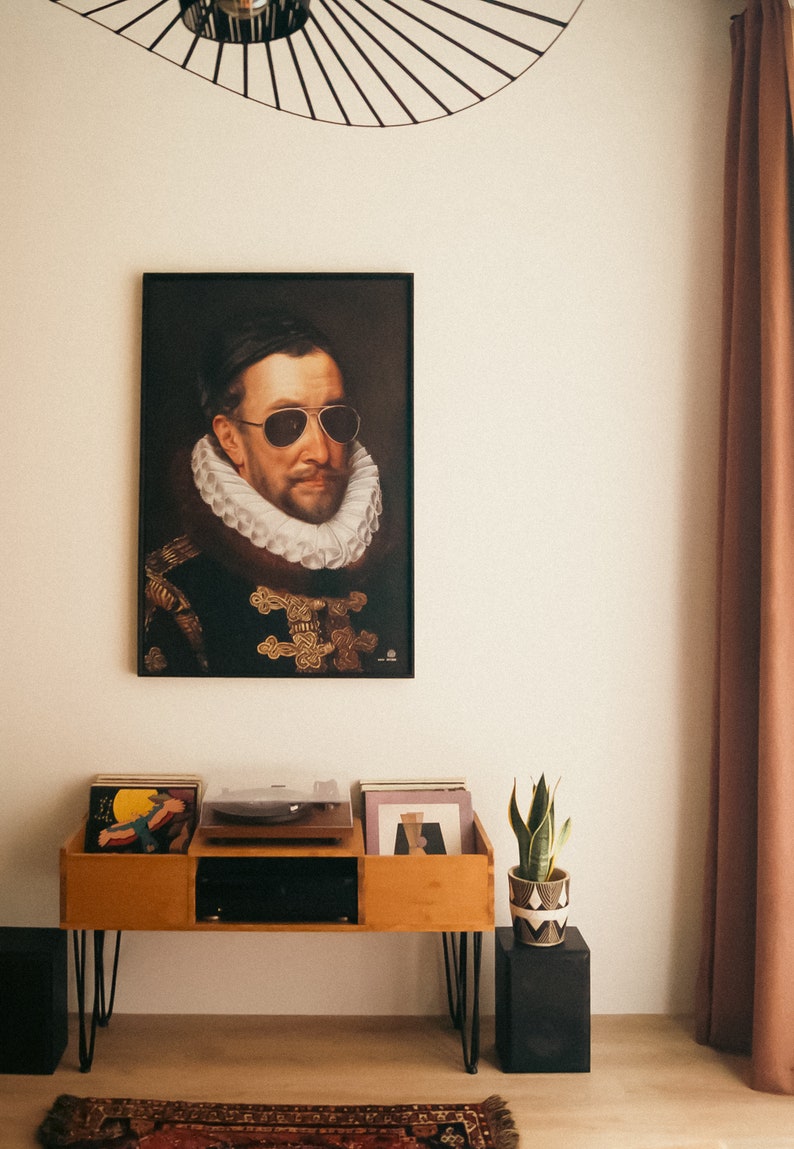 May include: A vintage-style portrait of a man wearing sunglasses and a large white collar, framed in black, hangs on a white wall above a wooden record player stand with a turntable and vinyl records. A potted snake plant sits on a black stand to the right of the record player.