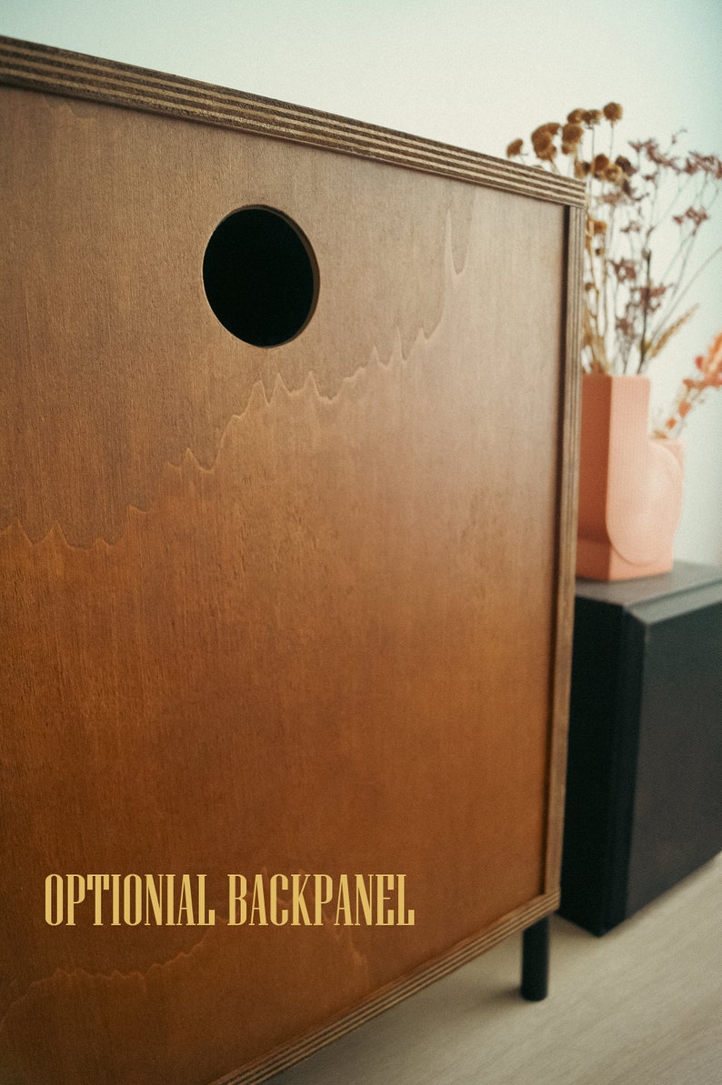May include: A wooden cabinet with a brown finish and a round hole in the back panel. The text "OPTIONAL BACKPANEL" is printed on the cabinet.
