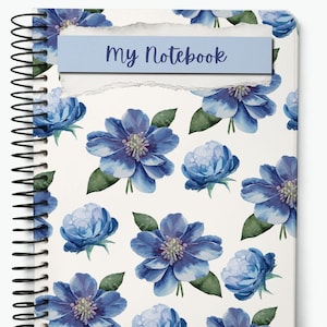 May include: Spiral-bound notebook with a floral design. The cover features a pattern of blue flowers with green leaves on a white background. A light blue banner with the text "My Notebook" is attached to the top.