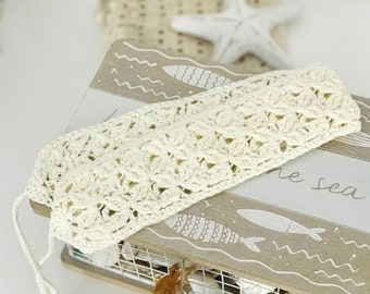 May include: A white crocheted headband with a delicate floral pattern. The headband is lying on a wooden box with a sea-themed design and the text "the sea".