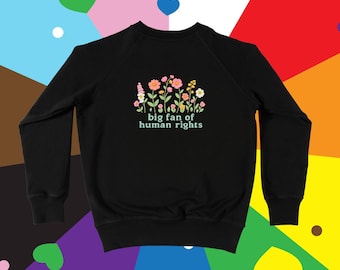 Puede incluir: Sudadera negra con un diseño floral y el texto "big fan of human rights" en blanco. El diseño floral incluye flores rosas, amarillas y naranjas con tallos y hojas verdes. El fondo es una colorida bandera del orgullo.