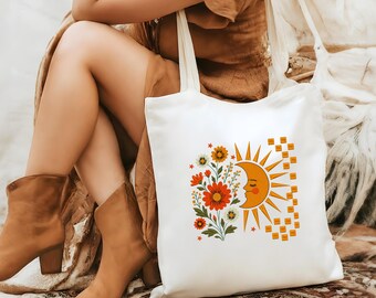 Puede incluir: Un bolso de tela blanco con un estampado gráfico colorido que muestra un sol creciente sonriente, un ramo de flores naranjas y rojas, y un pequeño patrón de cuadros. El diseño incluye pequeñas estrellas en la parte frontal.