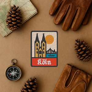 Może przedstawiać: Haftowana naszywka przedstawiająca Kolonię w Niemczech, z katedrą, mostem i słońcem. Naszywka ma czerwoną obwódkę i nazwę miasta „Köln” w kolorze białym. Naszywka otoczona jest kompasem, mapą, szyszkami i skórzanymi rękawicami.