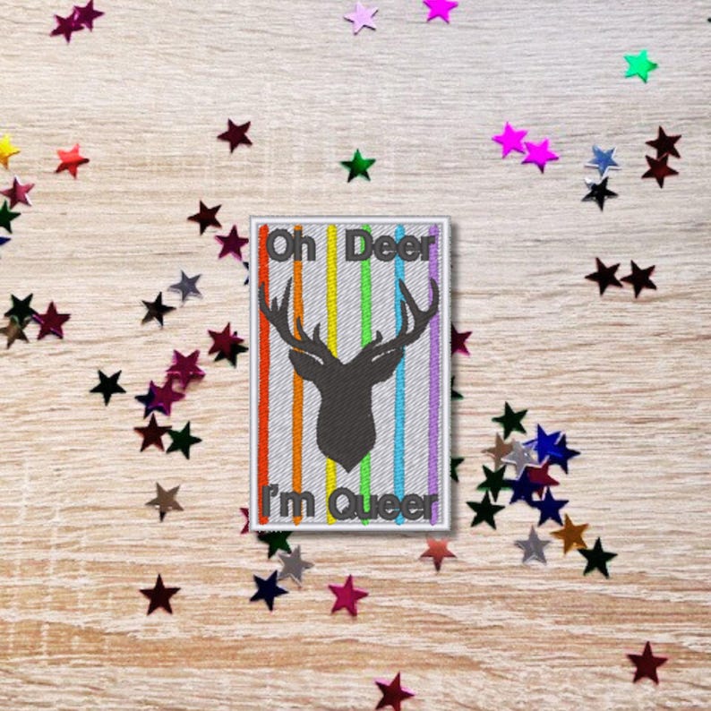 May include: A white rectangular patch with rainbow stripes and a black silhouette of a deer with antlers. The text "Oh Deer I'm Queer" is embroidered on the patch.