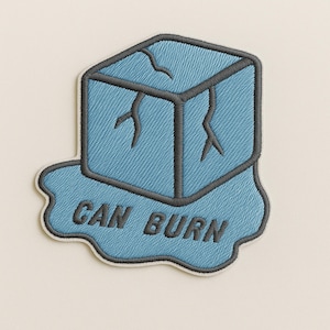 Può includere: Toppa ricamata raffigurante un cubetto di ghiaccio azzurro con contorni e crepe grigio scuro. La toppa presenta la scritta "CAN BURN" in grigio scuro, con una forma simile all'acqua azzurra sul fondo.