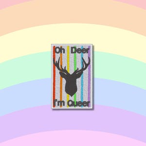 May include: A white embroidered patch with a rainbow stripe design and a black silhouette of a deer with antlers. The text "Oh Deer I'm Queer" is embroidered on the patch.