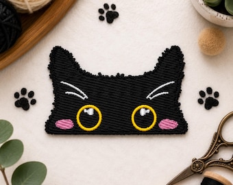 Puede incluir: Un parche bordado de una cara de gato negra con grandes ojos amarillos con reflejos blancos, mejillas rosadas y bigotes blancos. El parche tiene forma de cabeza de gato con orejas puntiagudas y está rodeado de pequeñas huellas bordadas en negro.