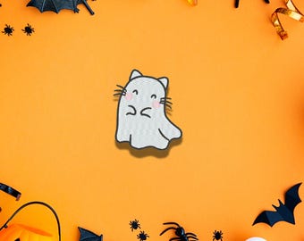 Puede incluir: Un parche bordado blanco con forma de fantasma con orejas de gato, bigotes y mejillas rosadas. El fantasma tiene una cara cosida simple con ojos cerrados y una boca pequeña, sobre un fondo de color naranja brillante y texturizado.