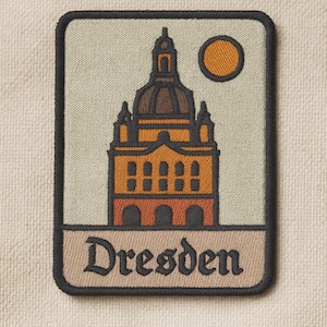 May include: Embroidered patch featuring a stylized illustration of a building with a dome, in shades of orange, brown, and beige, with a yellow sun. The word "Dresden" is written in a decorative font at the bottom.