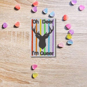 May include: A white patch with a rainbow stripe design and a black silhouette of a deer's head with antlers. The text "Oh Deer I'm Queer" is printed on the patch.
