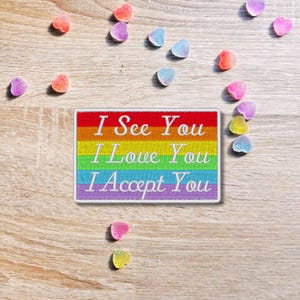 Pode incluir: Um remendo colorido do arco-íris com o texto "I See You I Love You I Accept You" em branco.